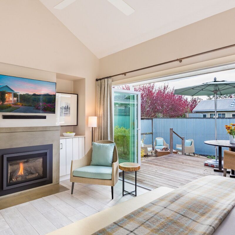 A cozy bedroom with a fireplace, armchair, and open patio doors leading to a deck with outdoor seating and an umbrella.